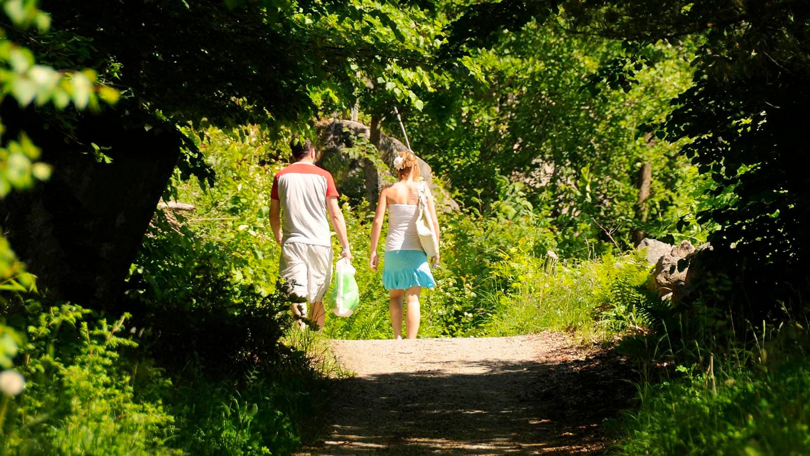 To personer går sammen langs Kjærlighetsstien på Hvaler, omgitt av grønn skog og sommerlys.