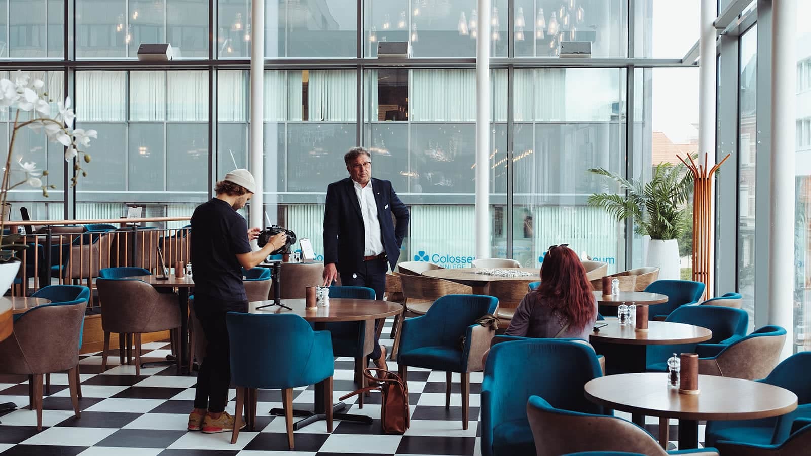 Filming i moderne restaurantlokale med intervjusituasjon, kameraoperatør og gjester.