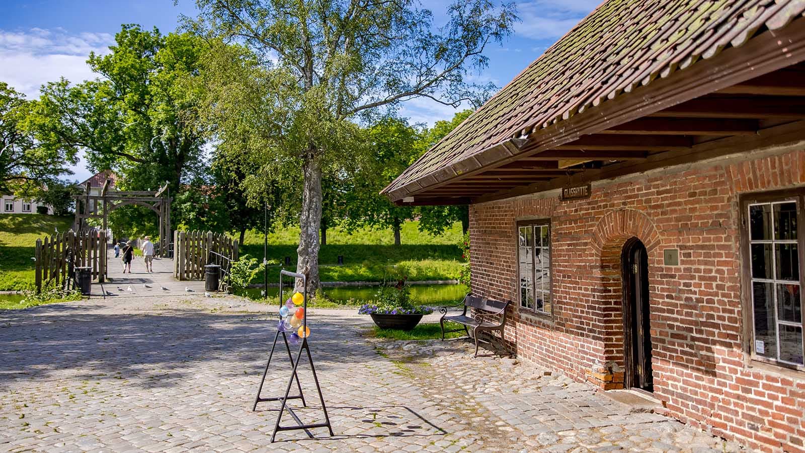 Utsikt mot Glasshytta og vindebrua i Gamlebyen, med kunstglass og grønt landskap i sommersol.