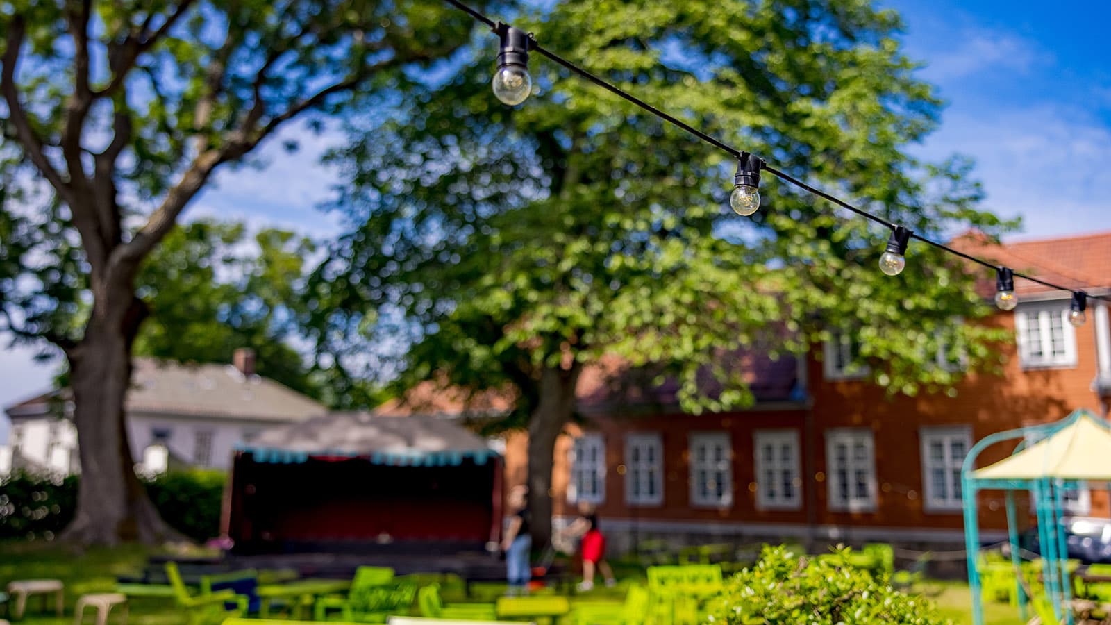 Utescene og hageområde med hagemøbler, trær og lysslynger i sommersol i Fredrikstad.